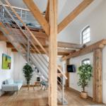 Wohnraum mit Holzdeckenbalken, Metalltreppe und Pflanzen.