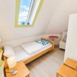 Ein Schlafzimmer mit Dachschräge, Bett, Stuhl, Tisch und Fenster.