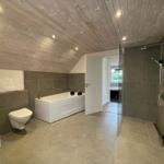 Badezimmer mit Badewanne, Dusche und Toilette unter Holzdecke.