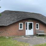Haus mit Strohdach, roten Ziegeln, weißer Tür und Bank vor dem Eingang.