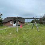 Haus mit Strohdach und Spielplatz mit Schaukel im Vorgarten.