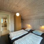 Zimmer mit zwei Betten, Holzwand und -decke, Nachttische und Lampen, Tür zum Bad.