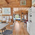 Holzhaus mit Essbereich, Wohnzimmer und Küchenzeile. Wand mit Kindergemälden und Karte.