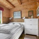 Schlafzimmer mit Holzwand, weißem Bett und Schrank. Fenster mit Blick auf grüne Vegetation.
