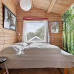 Schlafzimmer mit Holzwand, Bett, Fenster und Waldtapete.