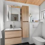 Badezimmer mit Holzregalen, Waschbecken und Toilette. Fenster und Spiegel sichtbar.