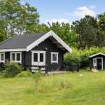 Schwarze Holzhütte mit weißen Fenstern und Terrasse im grünen Garten.