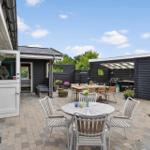 Terrasse mit Tisch, Stühlen und Grillbereich. Schwarze Holzwände und Pflanzen.