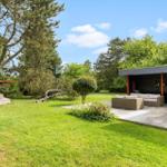 Deck with seating, large garden and trees under blue sky.