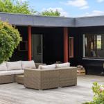 Terrace with seating, wooden planks, and garden. Black facade with windows.
