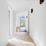 Hallway with wooden floor and window to terrace. White walls and wooden chair.