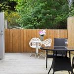 Deck with tables and chairs, wooden fence, and plants in the background.