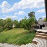 Wooden terrace with seating, view of green garden and trees under blue sky.