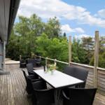 Deck with table and chairs, view of green trees under blue sky.