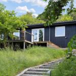 A dark blue house with a terrace and steps through grass. Surrounded by trees and greenery.
