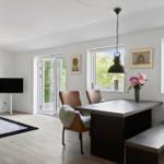 Dining area with table, chairs, and windows. Living area with sofa, TV, and hallway.