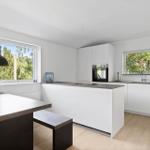 Modern kitchen with white cabinets, kitchen island, and windows with view of greenery.