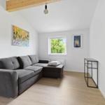 Living room with gray sofa, wooden floor, and window with view of trees.