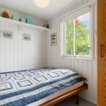 Schlafzimmer mit Bett, Fenster und Holzschränkchen. Wandverkleidung weiß, Decke weiß.