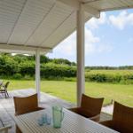 Terrasse mit Tisch und Stühlen, Grill und Blick auf grünes Feld.