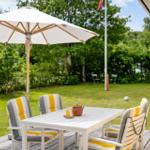 Terrasse mit Tisch, Stühlen und Sonnenschirm. Grasfläche mit Fußballtor im Hintergrund.