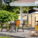 Terrasse mit Tisch, Stühlen und Liegestuhl. Hintergrund: Grünfläche und Holzhaus.