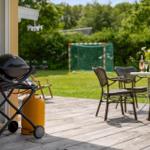 Terrasse mit Grill, Tisch und Stühlen. Im Hintergrund Fußballtor und Grünfläche.