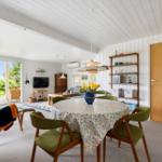 Esszimmer mit runden Tisch und grünen Stühlen. Hintergrund: Wohnbereich mit TV und Terrasse.