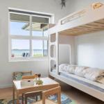 Kinderzimmer mit Doppelbett, Tisch und Fensterblick auf Wasser.