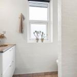 Badezimmer mit Waschbecken, Fenster und Pflanzen. Weiße Wände und Holzboden.