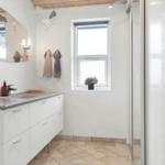 Badezimmer mit Waschtisch, Spiegel und Dusche. Fenster mit Blumen.