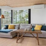Wohnzimmer mit Sofa, Holztisch und Blick auf Wald und Wasser.