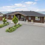 Ein Haus mit Terrasse und Blick aufs Wasser. Vorhof mit Pflanzen und Beete.