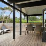 Terrasse mit Tisch, Stühlen und Liegen. Holzdecke und Sicht auf Bäume.
