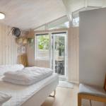 Schlafzimmer mit Bett, Holzwand und Terrassentür. Stuhl und Wanddekoration sichtbar.