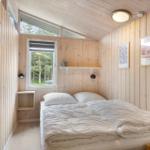 Schlafzimmer mit Holzwandverkleidung, Bett und Fenster zum Blick in den Wald.