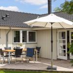 Deck with table, chairs, and umbrella in front of a house with wooden siding and roof.