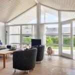 Living room with sofa, chairs, and fireplace. Large windows offer garden view.