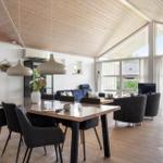 Dining area with table and chairs under wooden ceiling. Living area with sofa and TV. Large window front.