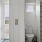 Bathroom with toilet, shower, and window. White walls and gray tiles.