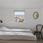 Two beds, window with view of a red house, chair and mirror on the wall.