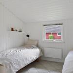 Two single beds, white paneled walls, window with view of red house.