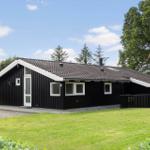 Black wooden house with white window frames and terrace. Green lawn and trees surround the house.