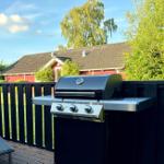 Gas grill on terrace with view of red house and green areas.