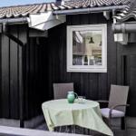 Outdoor terrace with table, two chairs, and green tablecloth. Black wooden wall and window.