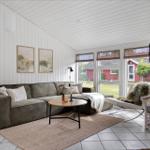 Living room with sofa, table, and chair. Windows show garden and red house.