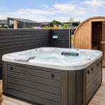 Außenwhirlpool mit Sauna auf Holzterrasse. Schwarze Holzwand im Hintergrund.