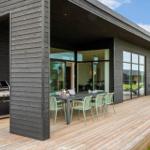 Terrasse mit Grill, Esstisch und Liegestühlen. Modernes Haus mit großem Glasbereich.