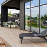 Terrasse mit Loungemöbeln, Tisch und Stühlen. Glasfront und Holzwände.
