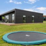 Moderne Villa mit Terrasse und Trampolin auf grünem Grundstück.